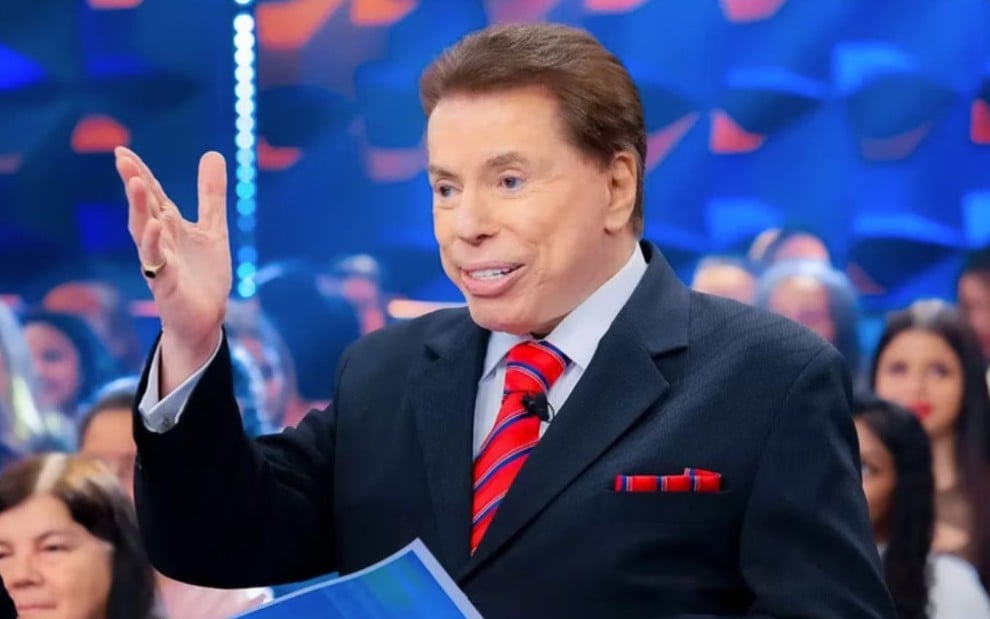 Silvio Santos está com uma mão estendida, no Programa Silvio Santos