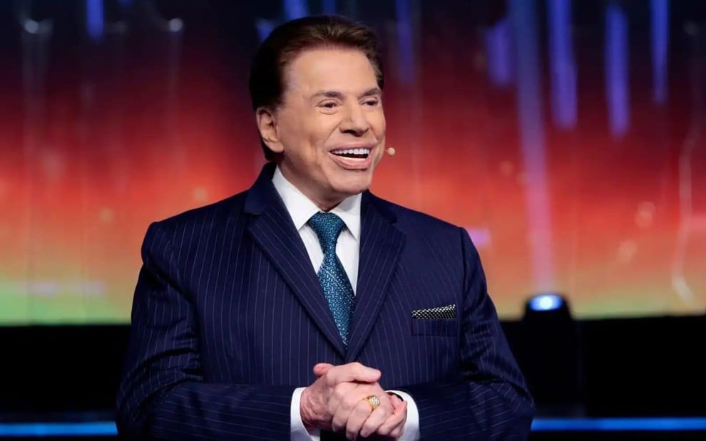 Silvio Santos usa um terno azul e está sorridente