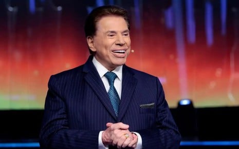 Silvio Santos usa um terno azul e está sorridente