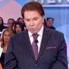 Foto de Silvio Santos durante programa; ele veste terno preto, camiseta branca e gravata roxa