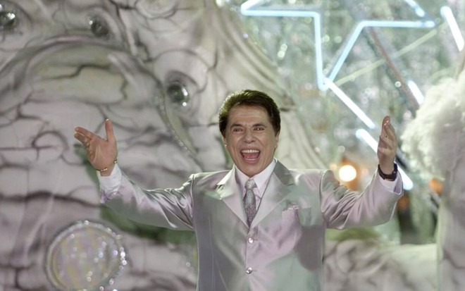 Silvio Santos abre os braços em cima de um carro alegórico
