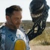 Com roupa de turista americano em férias, Tom Hardy parece triste e é observado por uma cabeça gosmenta de Venom