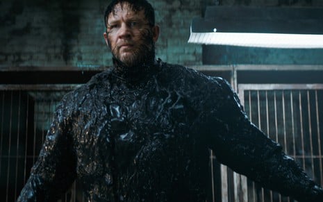 Tom Hardy está com os braços abertos e sendo tomado pela gosma gelatinosa preta do Venom