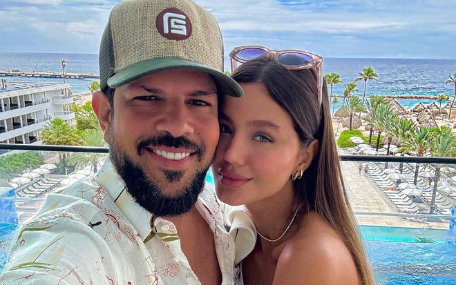 Sorocaba e Biah Rodrigues posam sorridentes diante de uma piscina de hotel