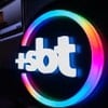 Logo do +SBT em gesso e com iluminação de LED; ao fundo, é possível ver uma projeção da interface da plataforma