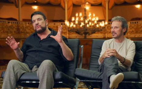 Michael Sullivan e Paulo Massadas em depoimento ao documentário do Globoplay sobre eles, sentados em cadeiras, com teatro ao fundo