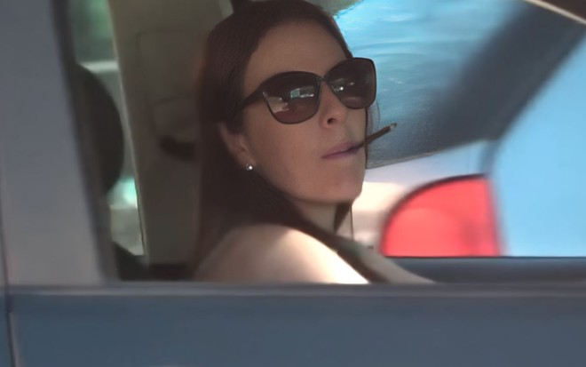 Suzane Richthofen está de óculos de sol e fuma cigarro dentro de um carro