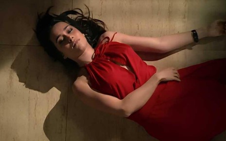 A atriz Alessandra Negrini deitada no chão, de olhos fechados, vestido vermelho, em cena de Paraíso Tropical