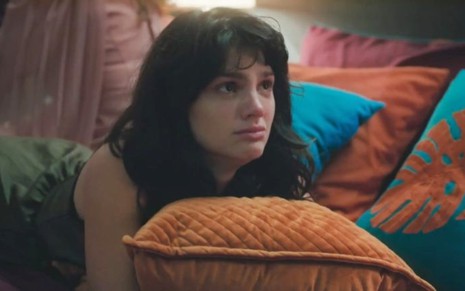 A atriz Debora Ozório em cena de Terra e Paixão, com expressão de tristeza deitada em cama
