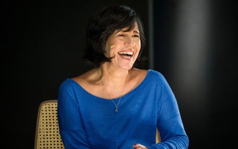 A autora Thelma Guedes, com uma roupa azul, em entrevista ao Ofício em Cena