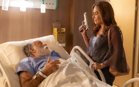 Antônio (Tony Ramos) está deitado em cama de hospital, Irene (Gloria Pires) aparece ao lado segurando arma em cena de Terra e Paixão