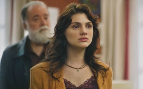 Debora Ozório com expressão séria em cena como Petra na novela Terra e Paixão; Tony Ramos aparece ao fundo