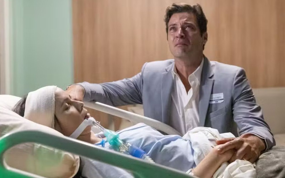 Marino (Leandro Lima) chora e olha para cima, enquanto Lucinda (Débora Falabella) está desacordada em cama de hospital em cena de Terra e Paixão