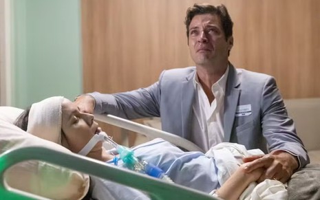 Marino (Leandro Lima) chora e olha para cima, enquanto Lucinda (Débora Falabella) está desacordada em cama de hospital em cena de Terra e Paixão
