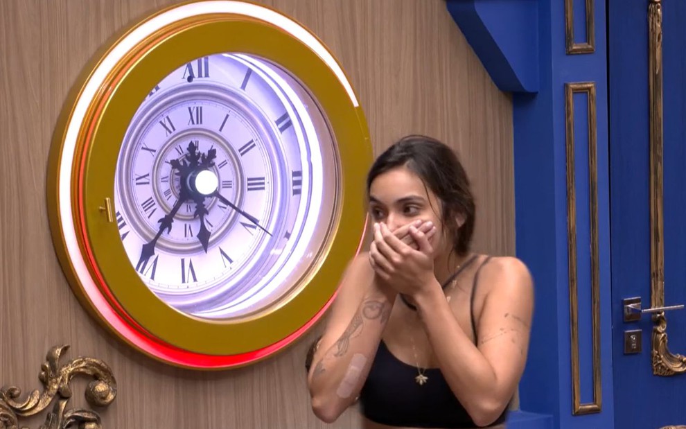 Vanessa Lopes está tapando a boca com as mãos e aparece parada na frente do botão da desistência do BBB 24