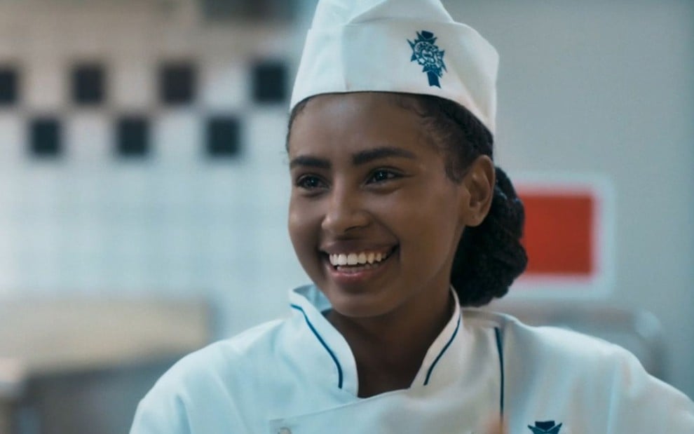 Gabz está sorridente em cena da novela Mania de Você; ela usa um uniforme de chef de cozinha