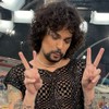 Vítor diCastro faz pose para foto no estúdio de vidro da Globo na Sapucaí; ele usa uma blusa transparente e maquiagem exagerada