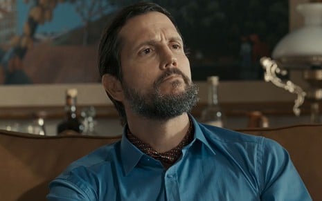 O ator Vladimir Brichta usa camisa azul e lenço colorido no pescoço em cena da novela Renascer como o vilão Egídio