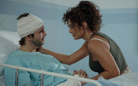 Vladimir Brichta está com a cabeça enfaixada numa cama de hospital, enquanto Juliana Paes coloca a mão no obro dele
