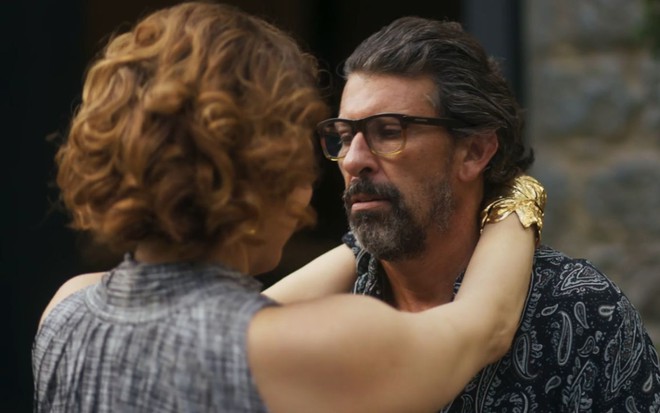 A atriz Isabel Teixeira, de costas, com as mãos em volta do pescoço do ator Milhem Cortaz, sério, em cena de Volta por Cima