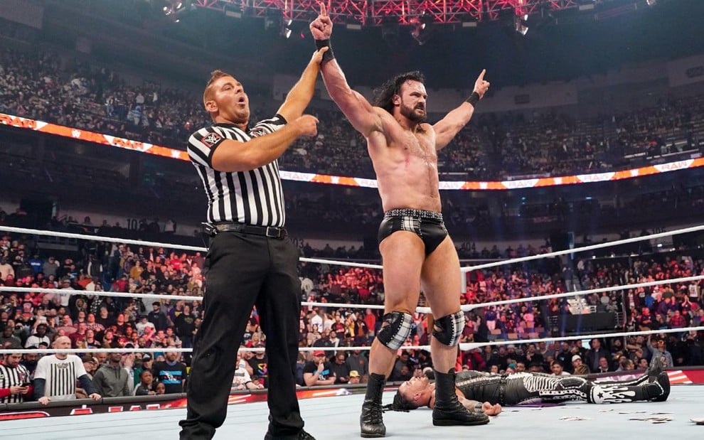 Juiz ergue os braços de Drew McIntyre em um ringue da WWE; Damian Priest está caído no chão