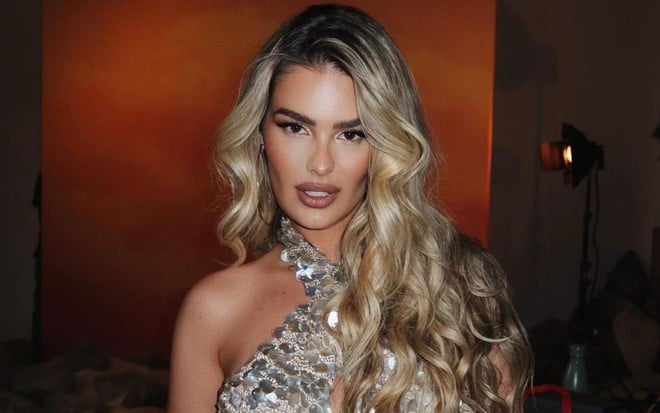 Yasmin Brunet sorri discretamente, com um vestido de lantejoulas prateado