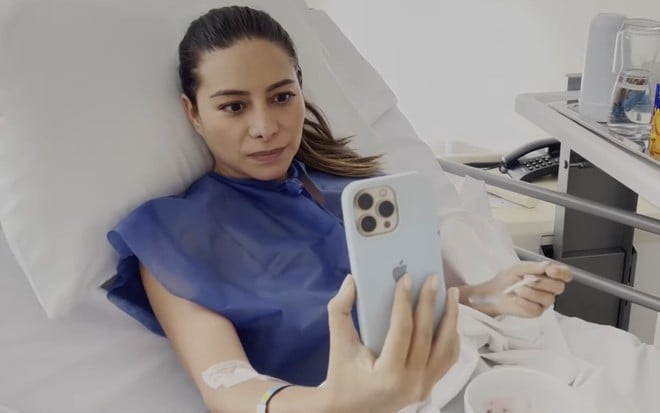 Marcela Monteiro está em uma cama de hospital, gravando vídeo no celular