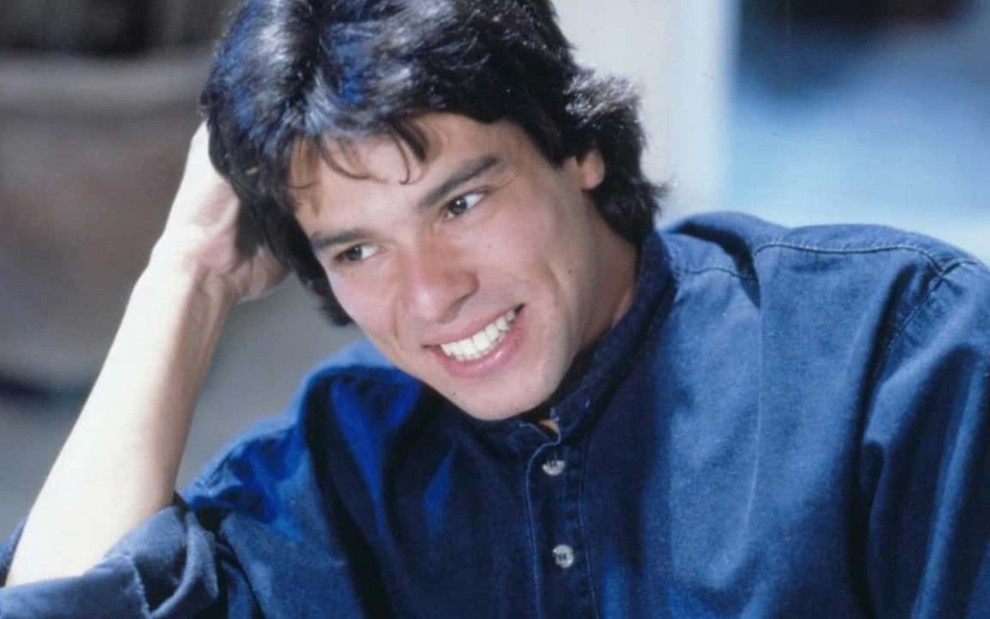 O ator Mauricio Mattar sorrindo, com mão na cabeça, em cena de A Viagem