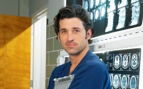 Patrick Dempsey posa com jaleco azul e encostado em parede com radiografias em Grey's Anatomy