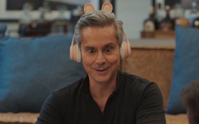 Alexandre Nero com expressão divertida em cena da novela Vale Tudo; ele usa um fone de ouvido rosa com orelhas de coelho