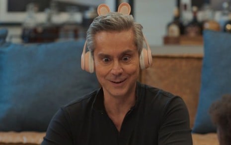 Alexandre Nero com expressão divertida em cena da novela Vale Tudo; ele usa um fone de ouvido rosa com orelhas de coelho