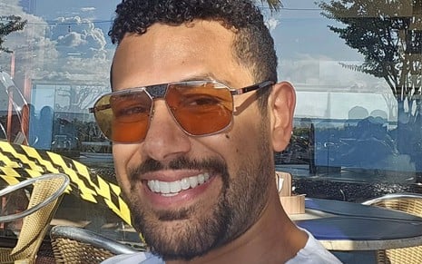 Amaury Lorenzo sorri e usa um óculos com lentes laranjas