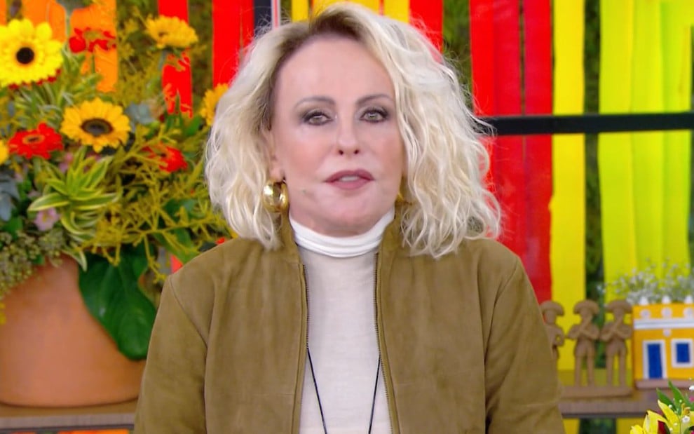 Ana Maria Braga no cenário do Mais Você, usando blusa de gola alta branca e jaqueta esverdeada