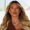Andressa Urach sentada em frente a uma janela, com feição séria, usando joias e cabelo loiro