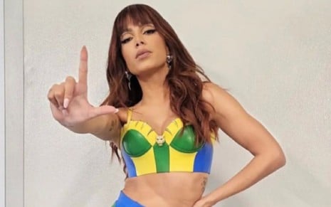 mulher morena veste um top com as cores da bandeira do Brasil e faz um L com a mão