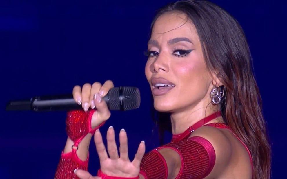 Foto mostra Anitta durante show; ela usa figurino vermelho e segura microfone