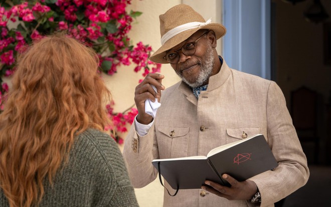 Samuel L. Jackson faz um aceno de cabeça com a mão em um chapéu, para uma mulher ruiva que está de costas para a câmera