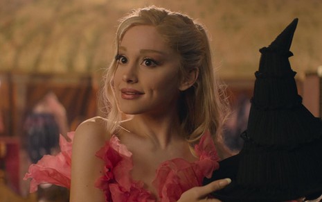 Ariana Grande segurando um chapéu de bruxa em cena de Wicked