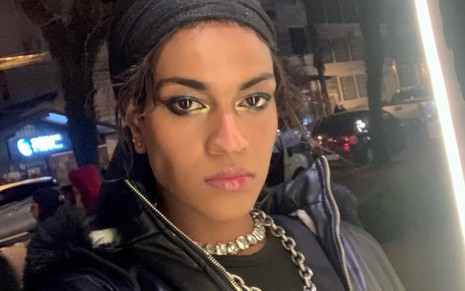 Ayla Gabriela posando, à noite, em foto para o Instagram; ela usa faixa preta no cabelo e maquiagem dourada e preta