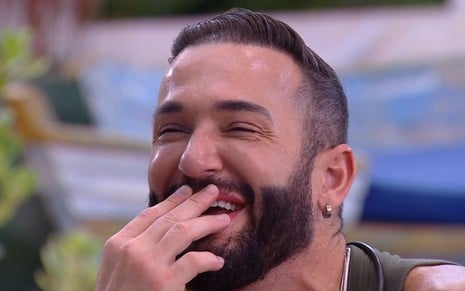 Diego Hypolito está com as mãos sobre a boca e gargalha no BBB 25