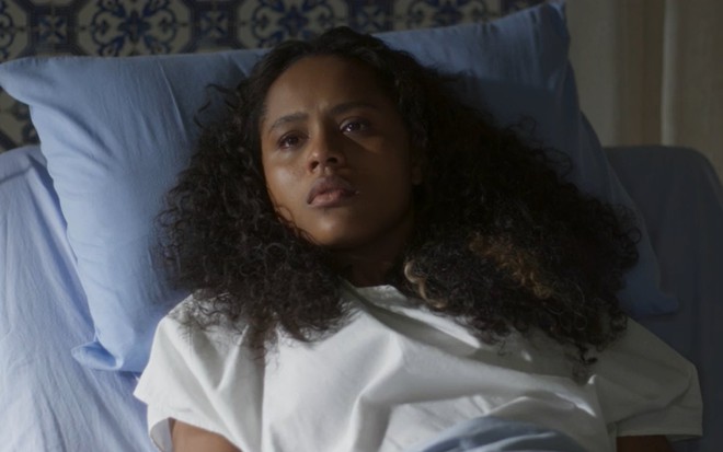 Duda Santos está deitada em cama de hospital, com expressão de doente