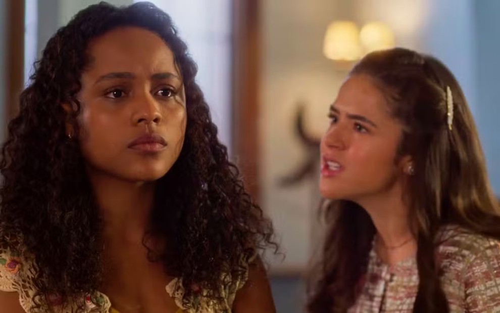 A atriz Duda Santos séria, olhando para frente, e a atriz Maisa olhando para ela com raiva, em cena de Garota do Momento