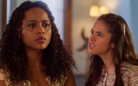 A atriz Duda Santos séria, olhando para frente, e a atriz Maisa olhando para ela com raiva, em cena de Garota do Momento