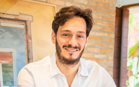 Homem branco, de cabelos e barba pretos, usando camisa branca