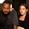 Bruno Monteiro e Tati Machado lado a lado em um estúdio fotográfico, os dois usam roupas pretas e olham para uma tela; ela segura no ombro dele