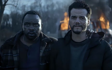 Bryan Tyree Henry e Wagner Moura caracterizados como Ray e Manny, na série Ladrões de Drogas, do Apple TV+; os dois se abraçam em frente a um incêndio