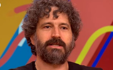 Caco Ciocler está com expressão séria e usa uma camiseta preta