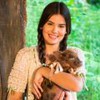 Camila Queiroz está com duas tranças nos cabelos e segura uma porquinha no colo