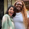 A atriz Carol Castro com expressão muito feliz ao lado da cantora Liniker na cidade cenográfica de Garota do Momento