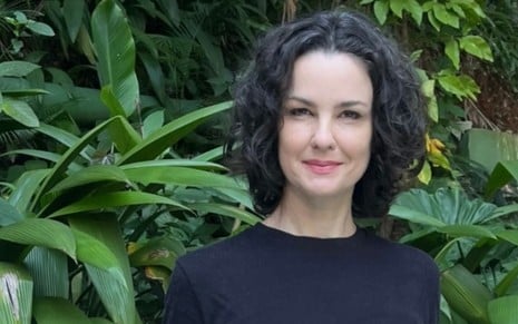 mulher morena posa para foto em cenário de natureza; ela veste roupas azuis